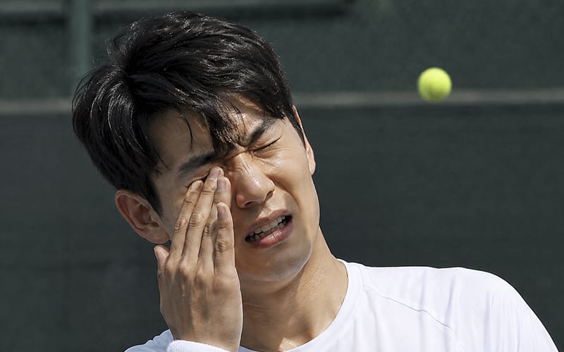 A young man in his 20s or 30s in pain after being hit in the eye with a sports ball