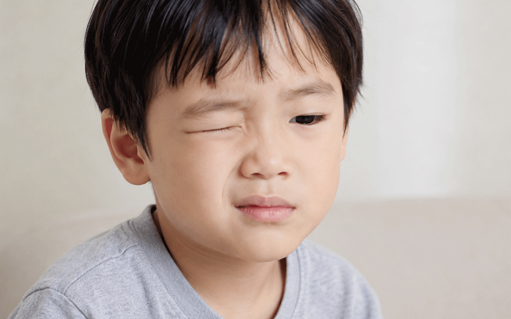 A child grimacing with one eye closed in discomfort