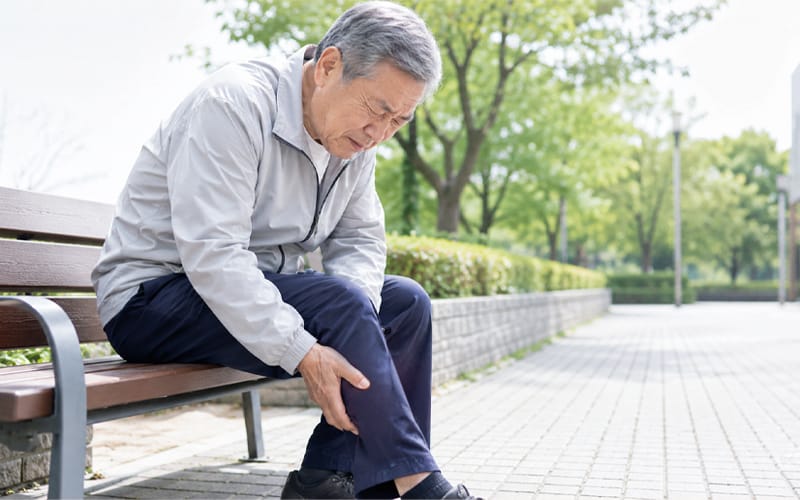 An elderly patient sitting on a bench holding their leg in pain