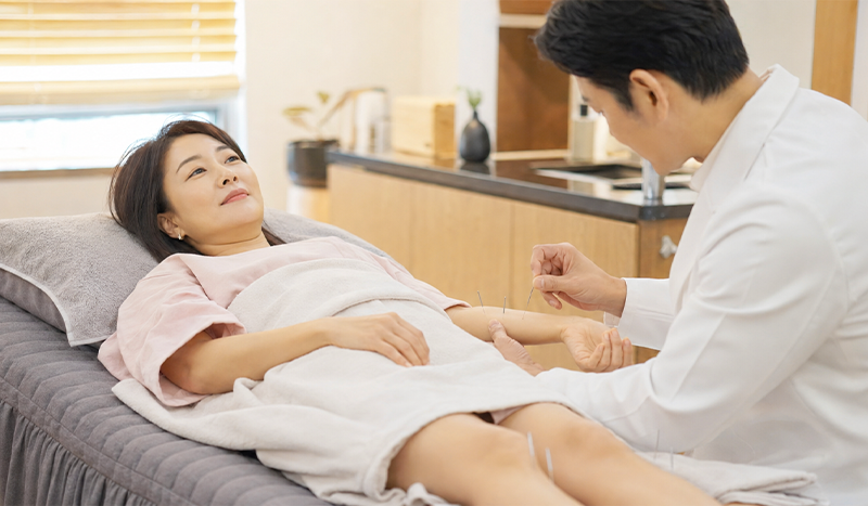 A woman in her early 40s receiving acupuncture treatment at a traditional medicine clinic