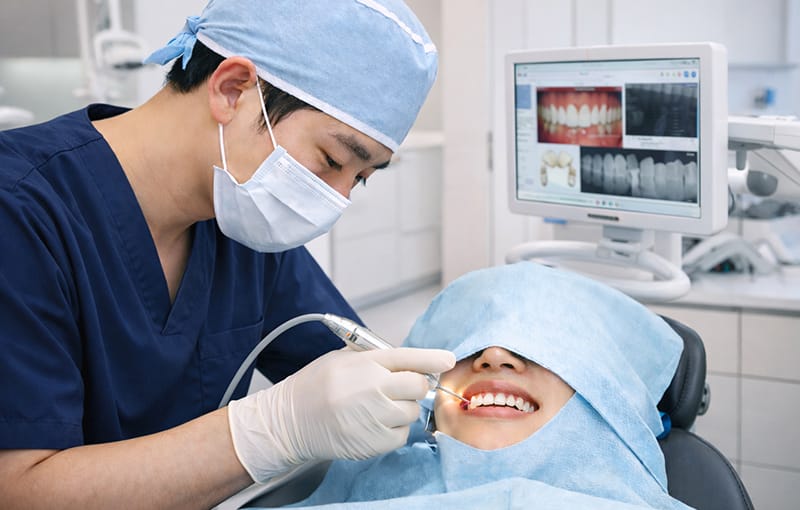 A dentist performing a veneer procedure while reviewing a patient's dental data